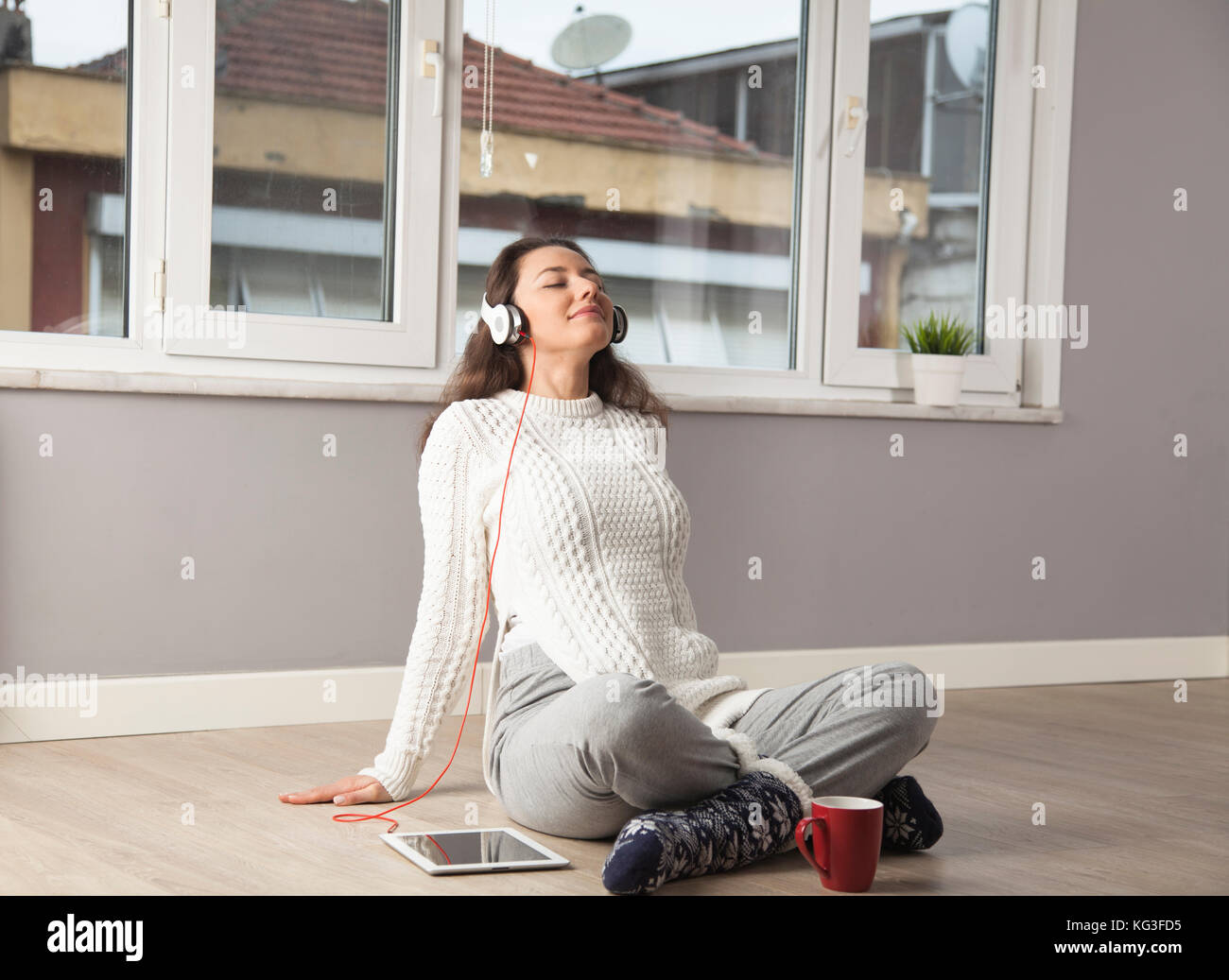 Happy young woman listening to music while sitting on the floor at home ...