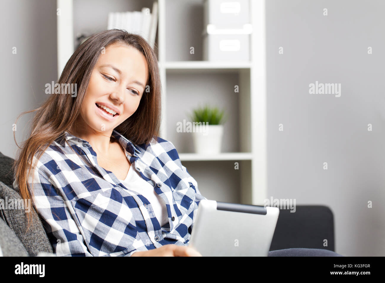 Young woman sitting on sofa in living room and using tablet Stock Photo ...