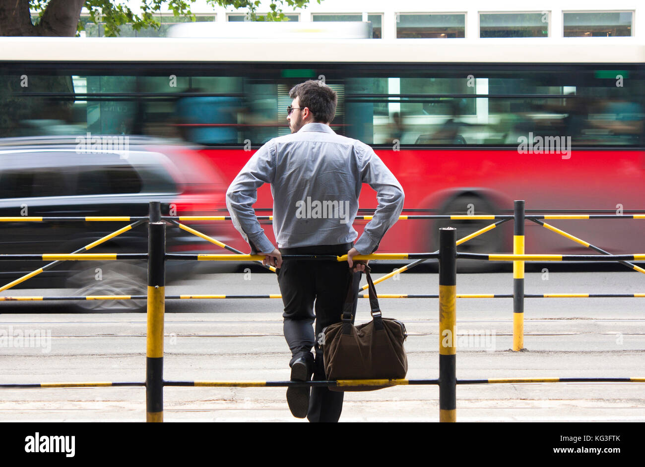 Belgrade, Serbia - June 21, 2017: Young man waiting at bus stop  leaned on the railings in the middle of the street , with city traffic in background  Stock Photo