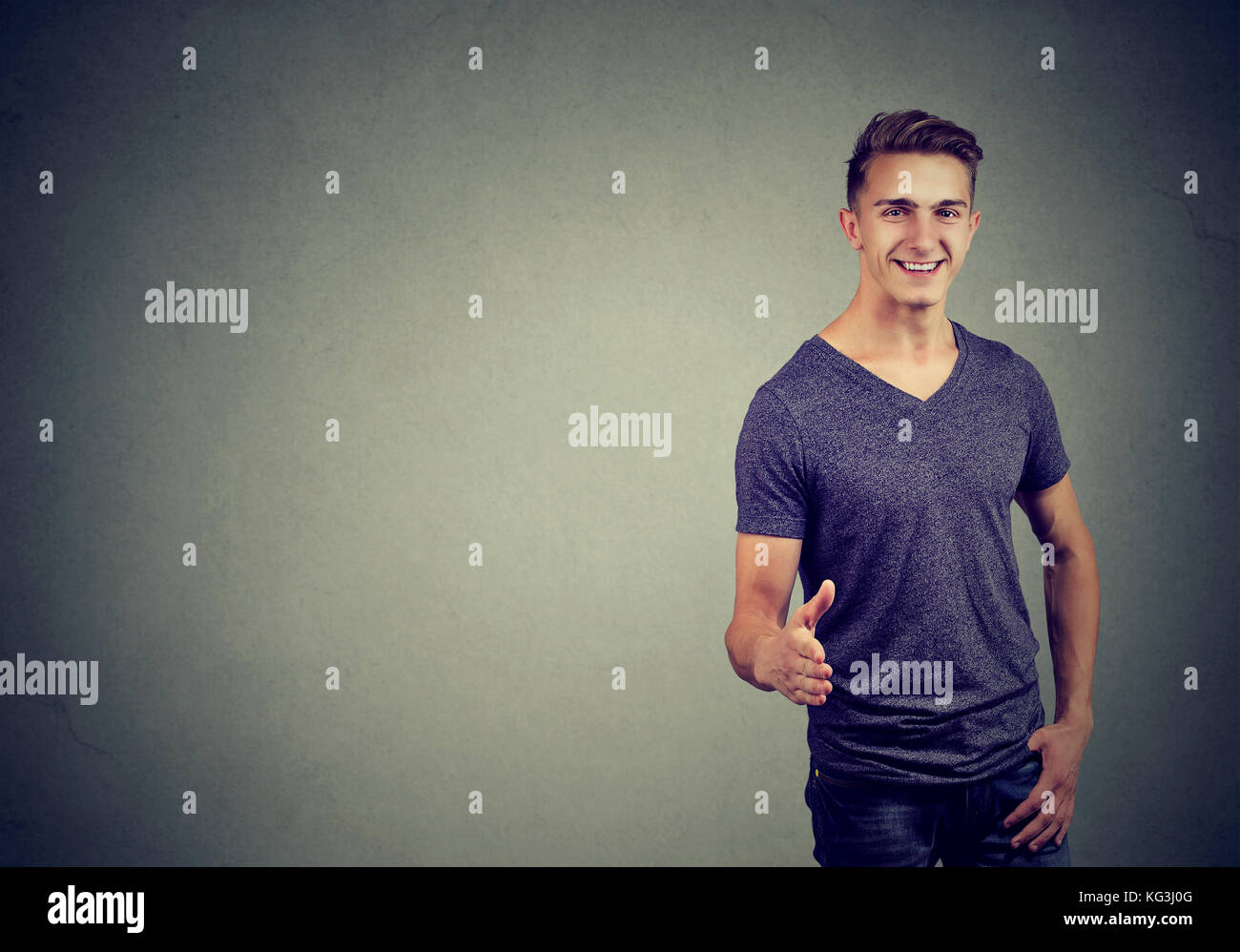 Smiling man in t-shirt holds out his hand for a handshake and looking at the camera over gray background Stock Photo