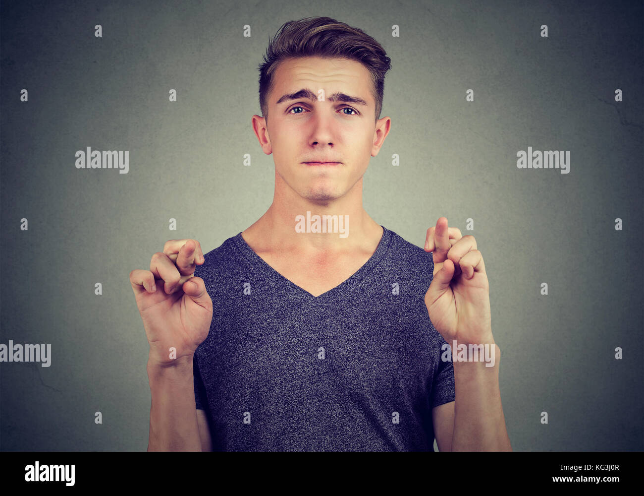 Hopeful man crossing his fingers hoping isolated on gray wall background. Human emotions, feelings reaction Stock Photo