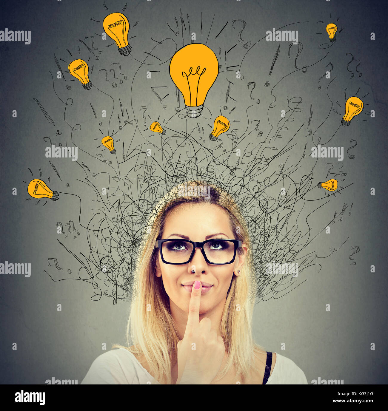 Brain connections. Happy thoughtful woman looking up at many ideas light bulbs above head isolated on gray wall background. Eureka concept Stock Photo