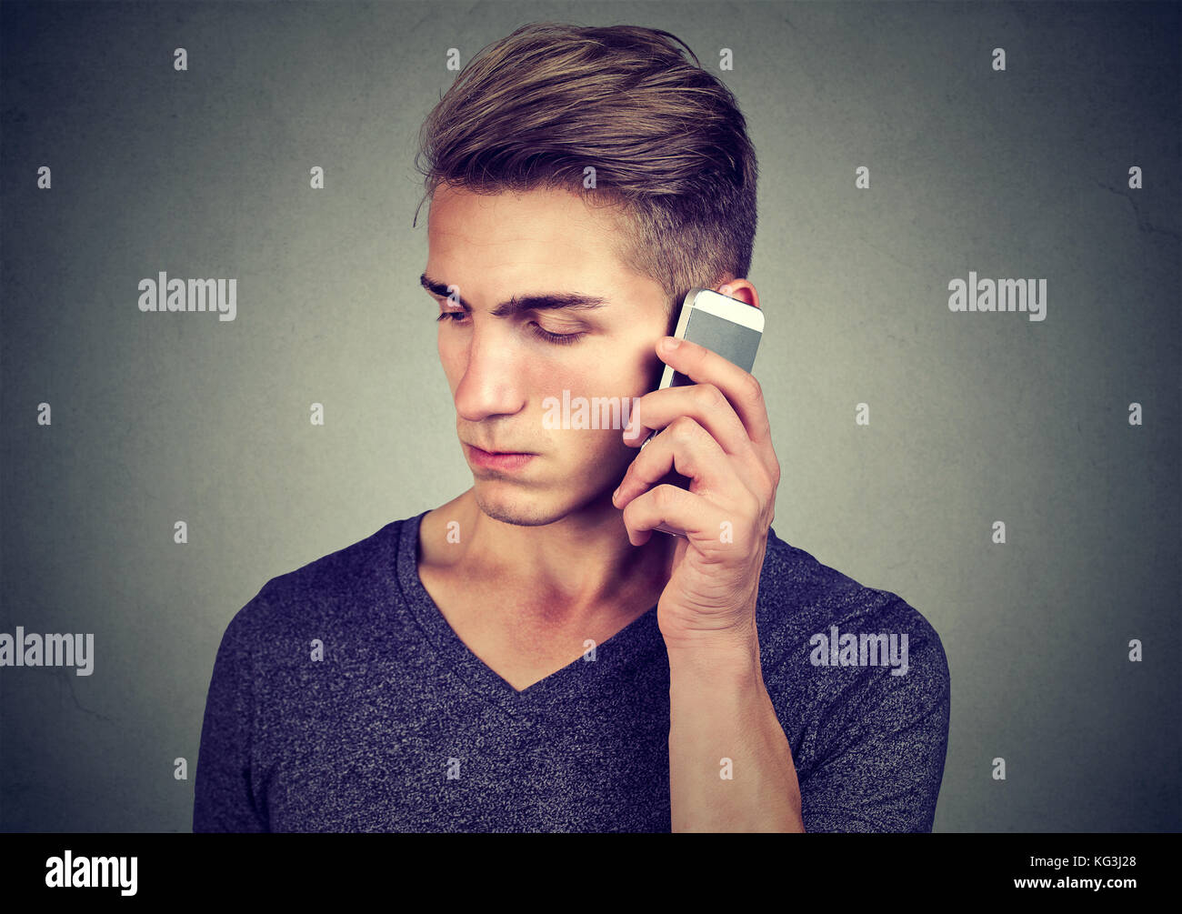 Man on the cellphone with headache. Upset unhappy guy talking on phone isolated on gray background. Negative human emotion face expression feeling lif Stock Photo