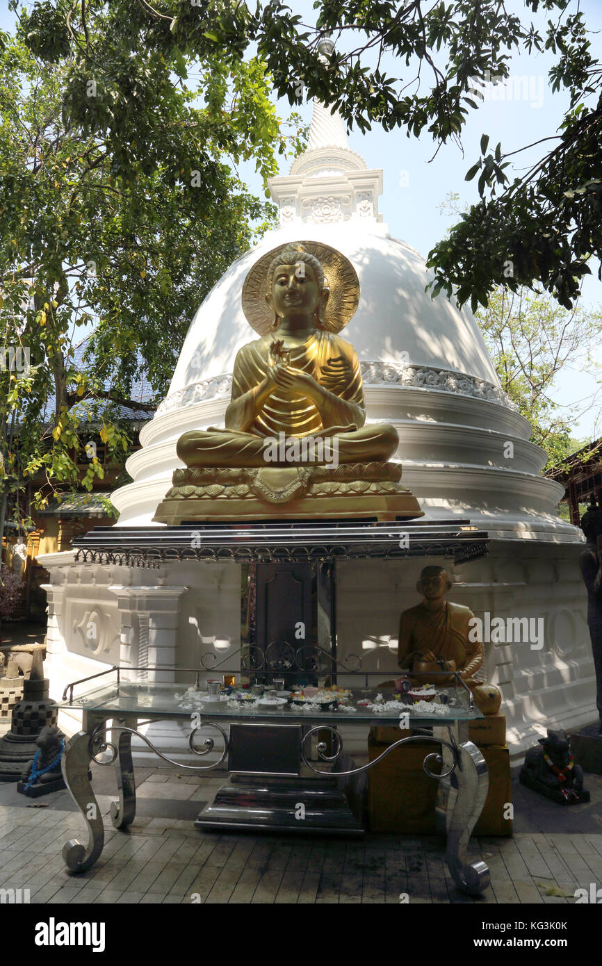 Colombo Sri Lanka Slave Island Gangaramaya Temple Gold Buddha Statue with the Dharmachakra Mudra and seated in the Padmasana Position in front of Dago Stock Photo