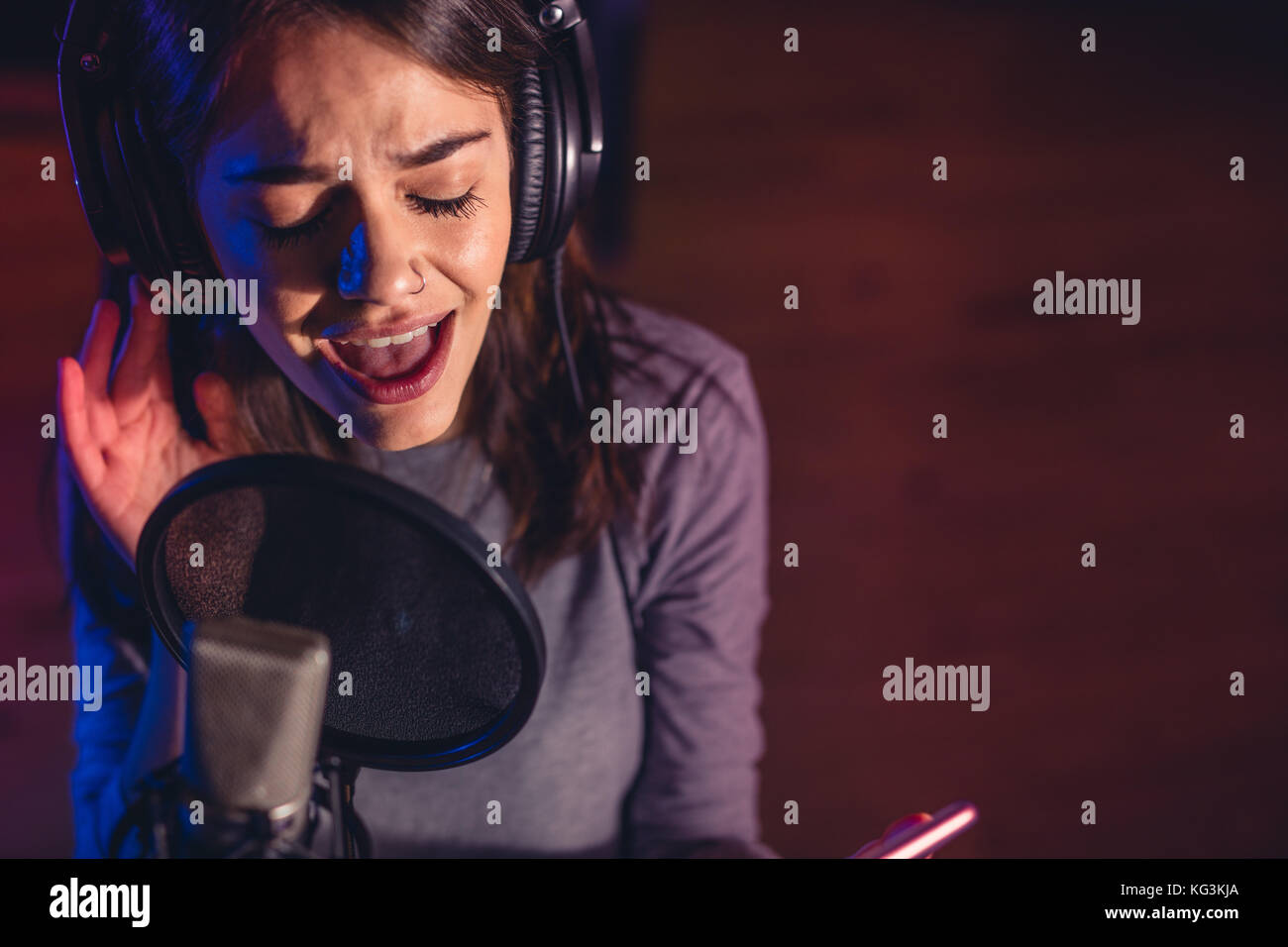 Close up of female singer singing in a microphone. Young woman music artist singing a song in the recording studio. Stock Photo