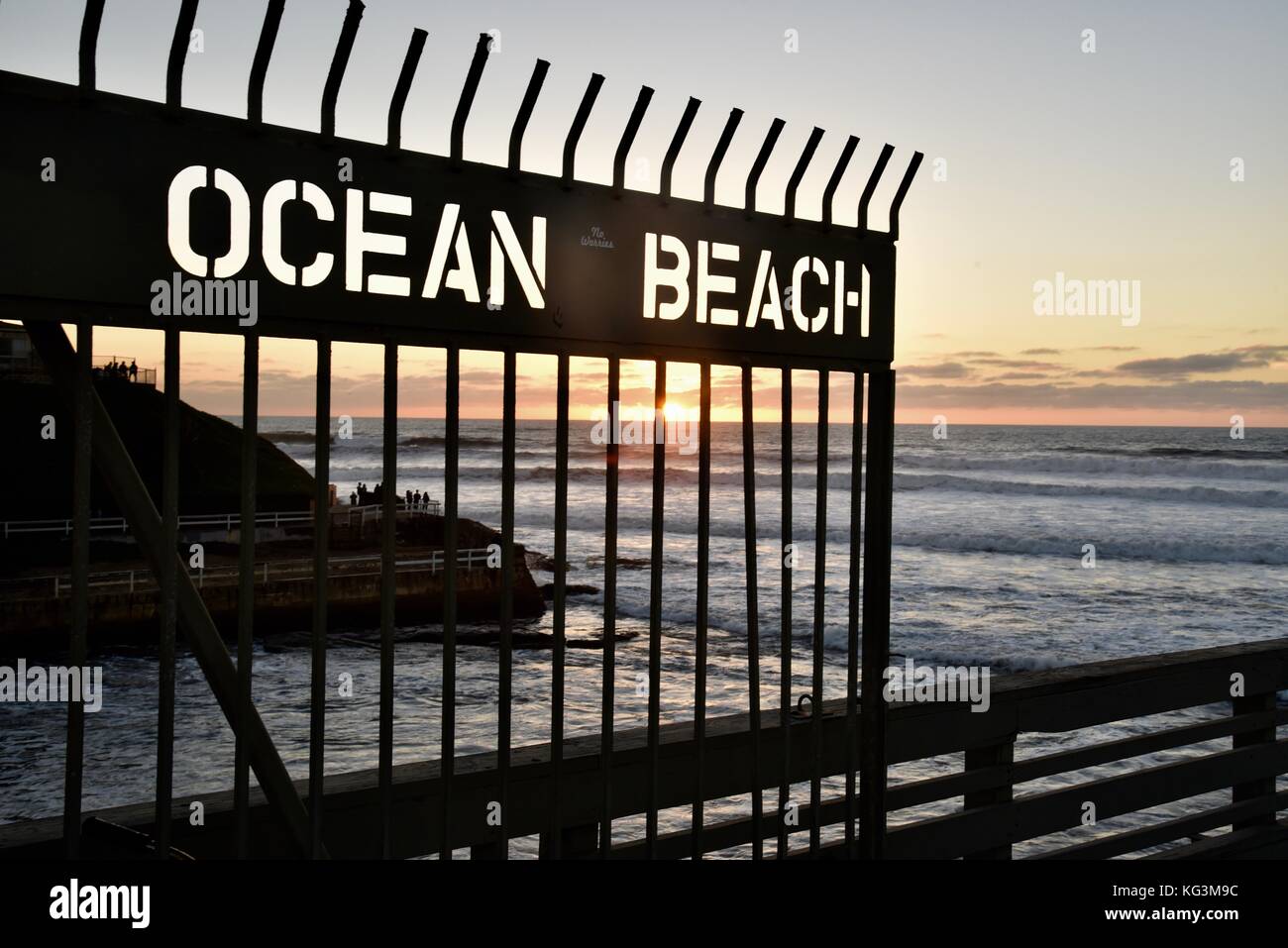 Gate at pier at Ocean Beach during sunset with high waves crashing on pier, San Diego, California USA Stock Photo