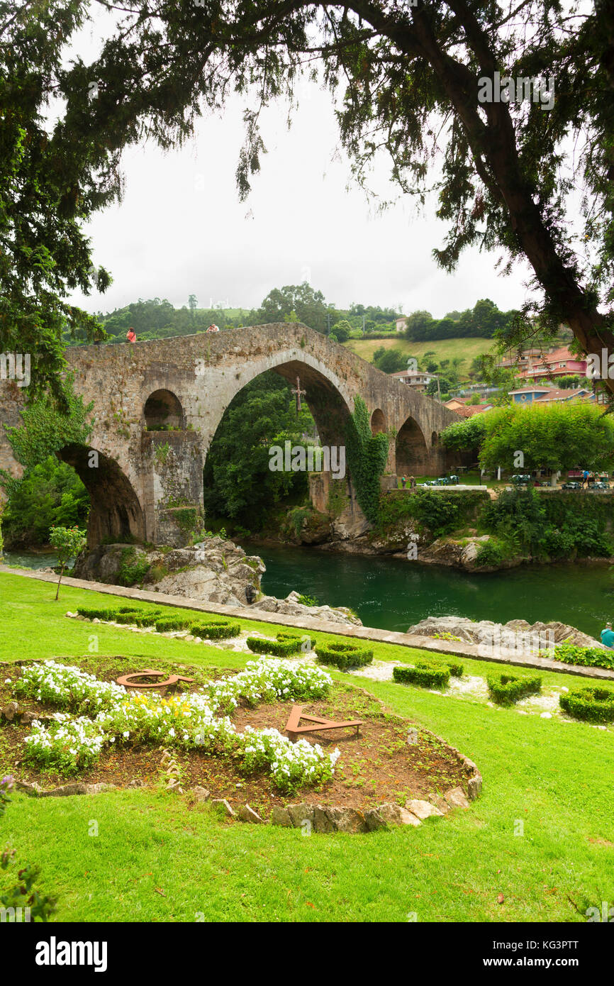 Puente Romano in Cangas de Onis. Summer day, a view from the coast through branches of trees