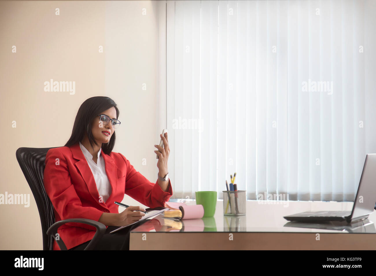 Businesswoman holding cell phone writing in notebook Stock Photo
