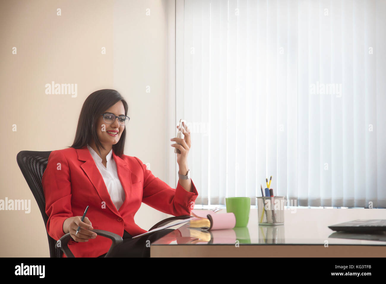Smiling businesswoman holding cell phone writing in notebook Stock Photo