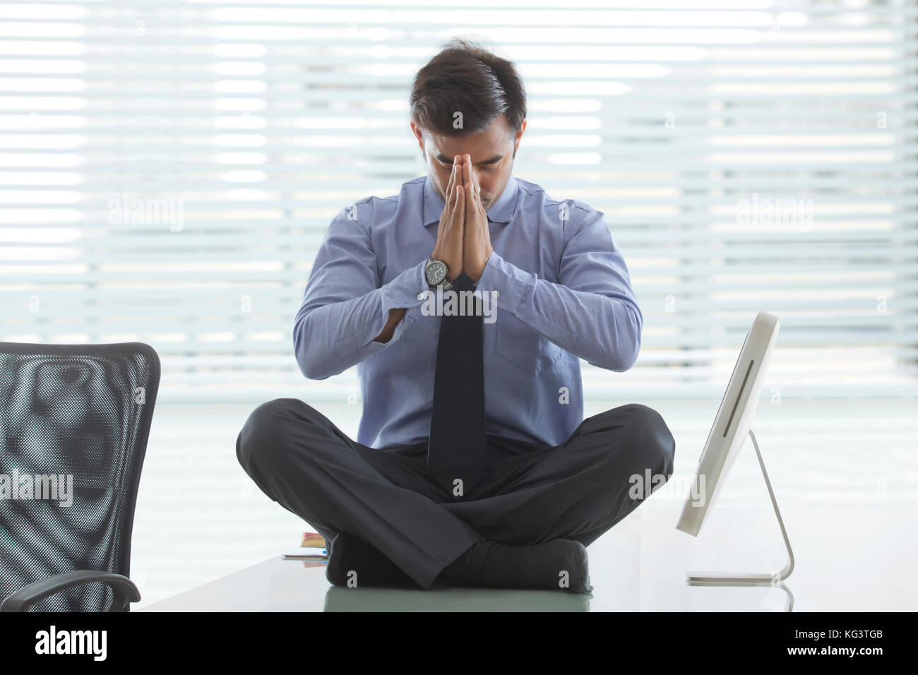 Businessman meditating on desk in office Stock Photo