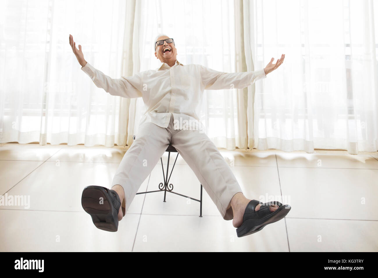 Happy old man sitting in chair with arms and legs outstretched Stock Photo