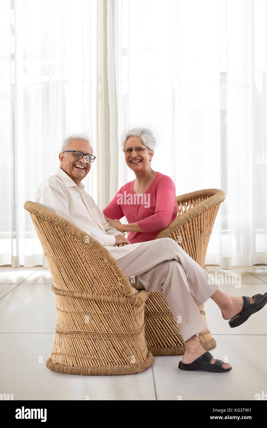 Portrait of smiling senior couple sitting on wicker chair at home Stock Photo