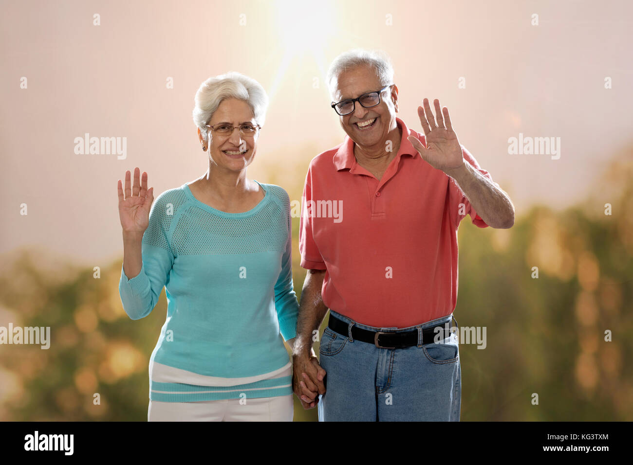 Smiling senior couple standing outdoors in nature and waving hands Stock Photo