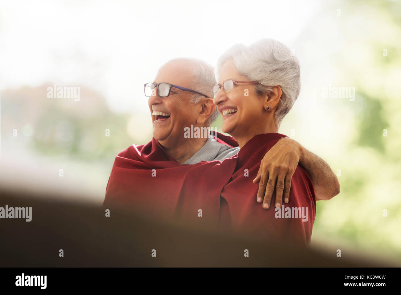 Happy senior couple wrapped in blanket sitting outdoors Stock Photo