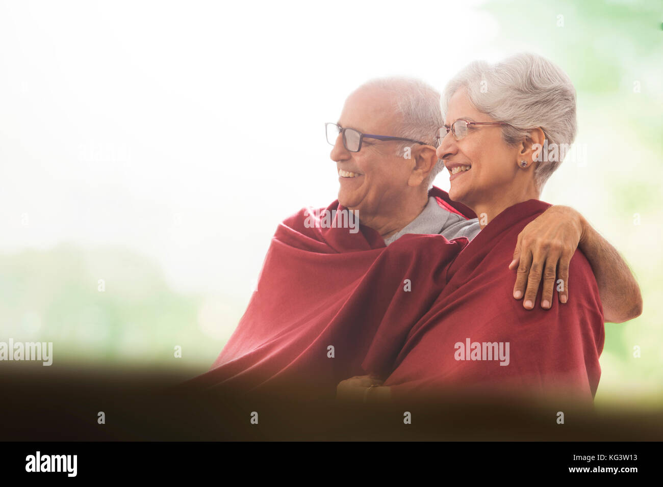Smiling senior couple wrapped in blanket sitting outdoors Stock Photo