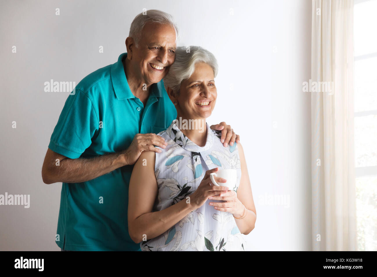 Smiling senior couple looking through window while having tea Stock Photo
