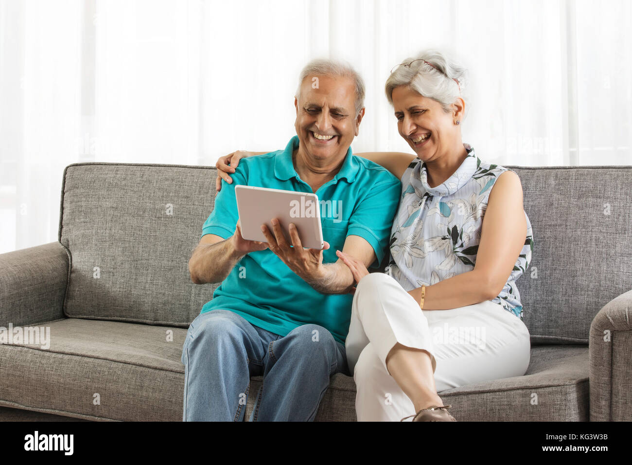 Senior couple sitting on sofa using digital tablet Stock Photo