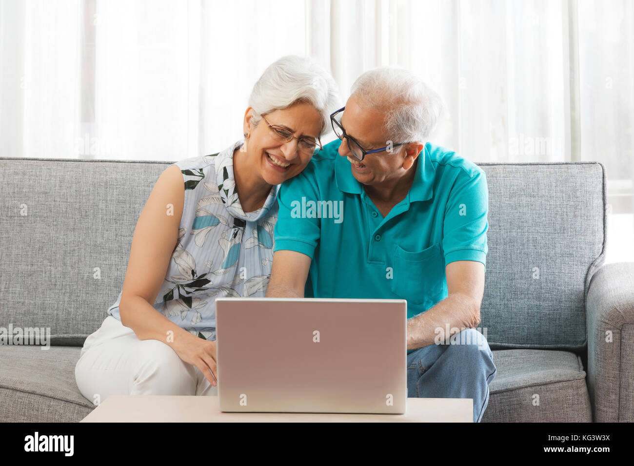 Smiling senior couple using laptop sitting on sofa Stock Photo