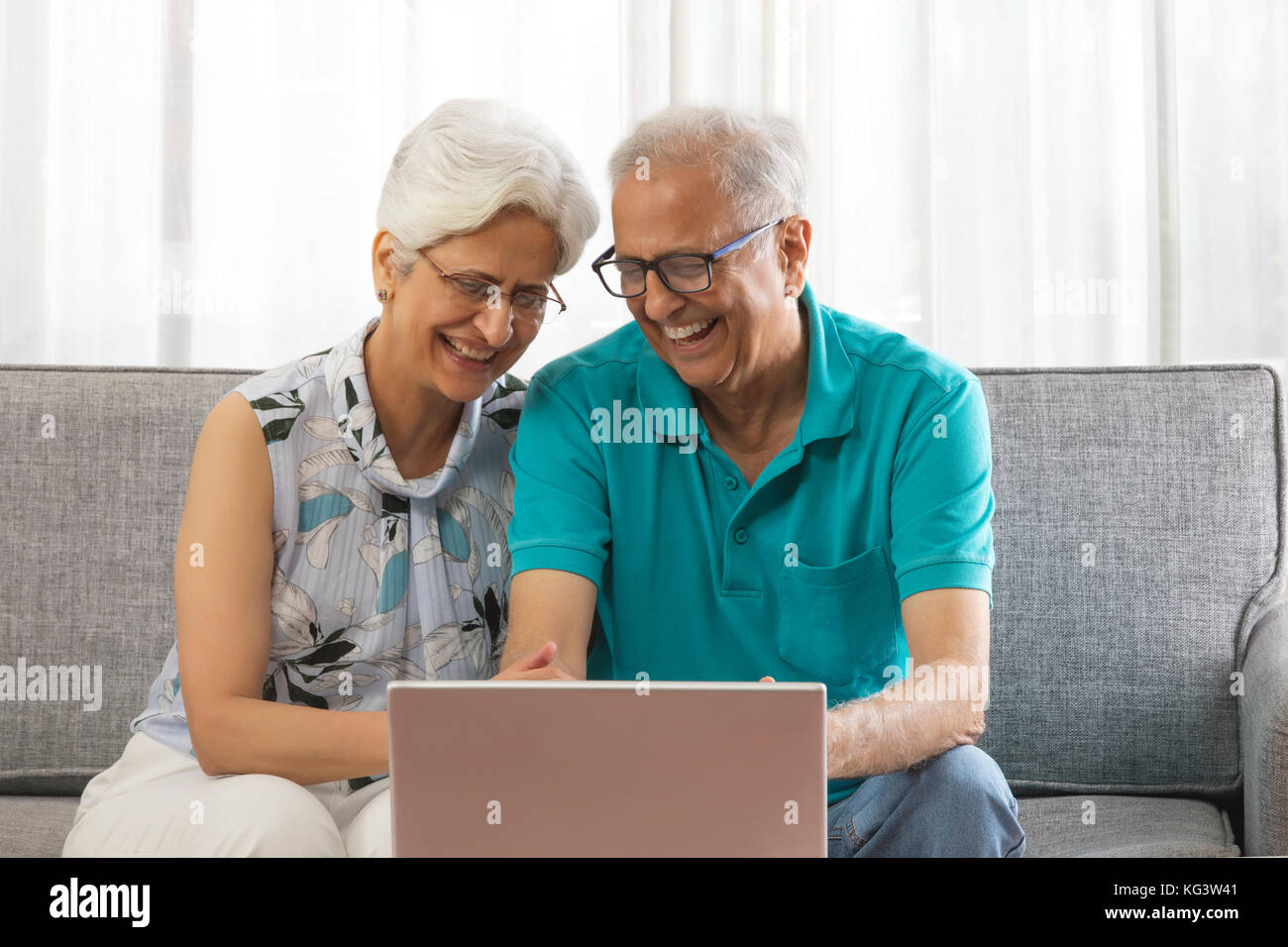 Happy senior couple using laptop sitting on sofa Stock Photo