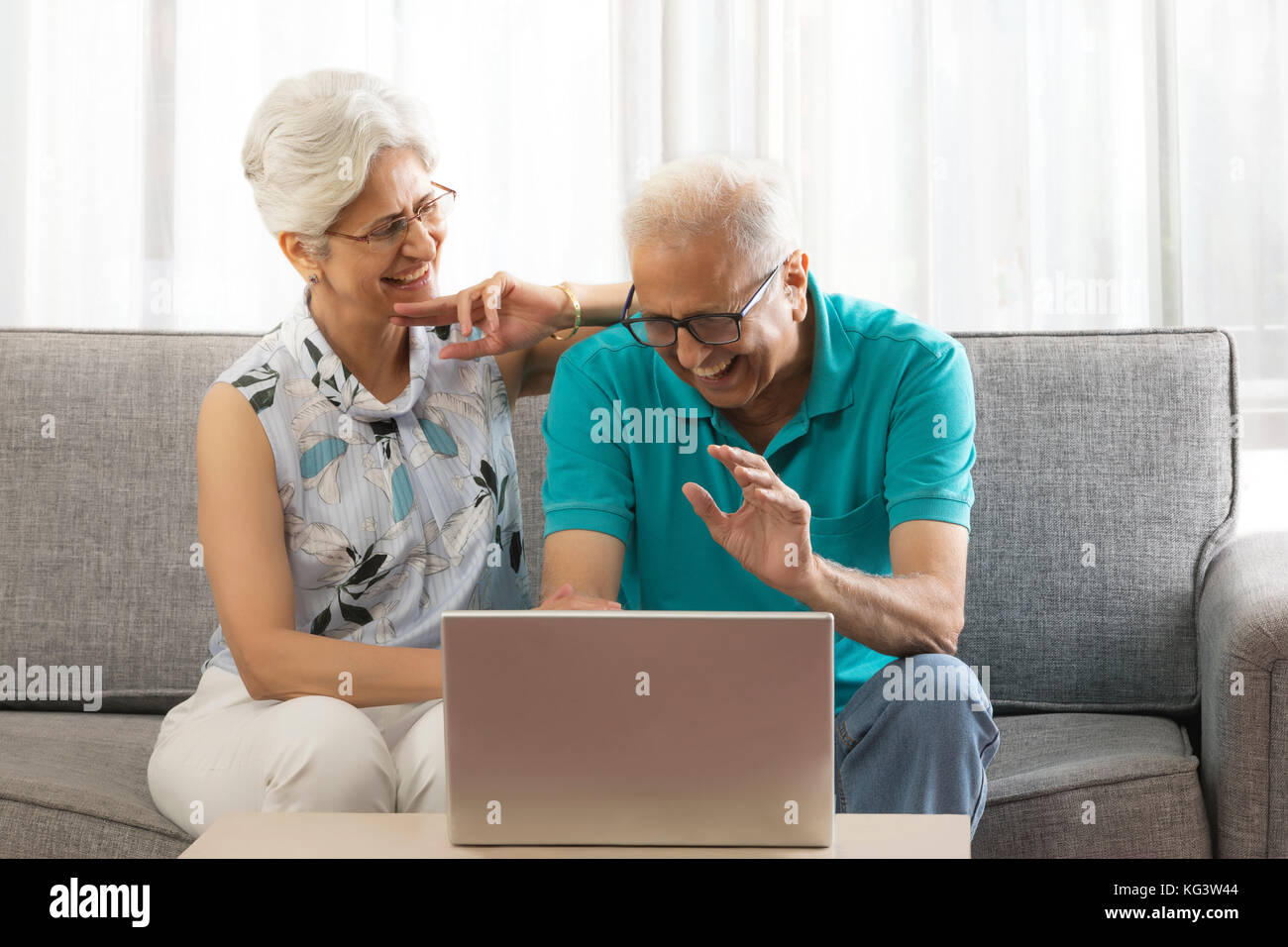 Smiling senior couple using laptop sitting on sofa Stock Photo