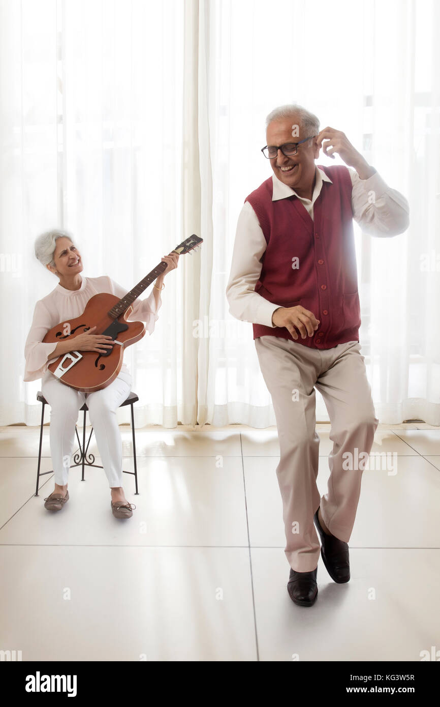 Senior woman playing guitar and senior man dancing Stock Photo
