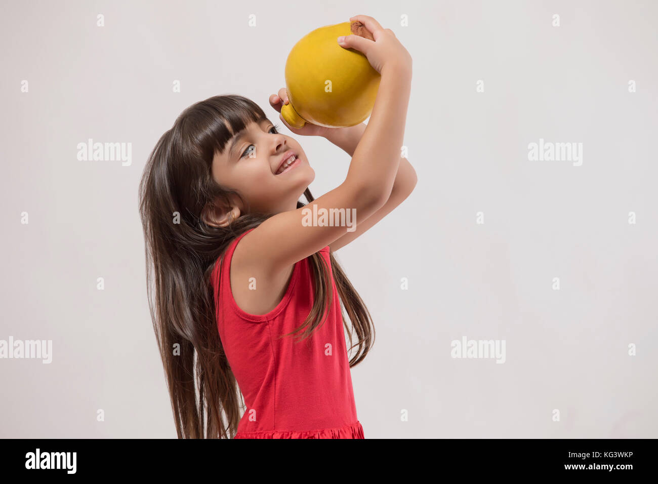 Girl looking at piggy bank while standing against white background Stock Photo
