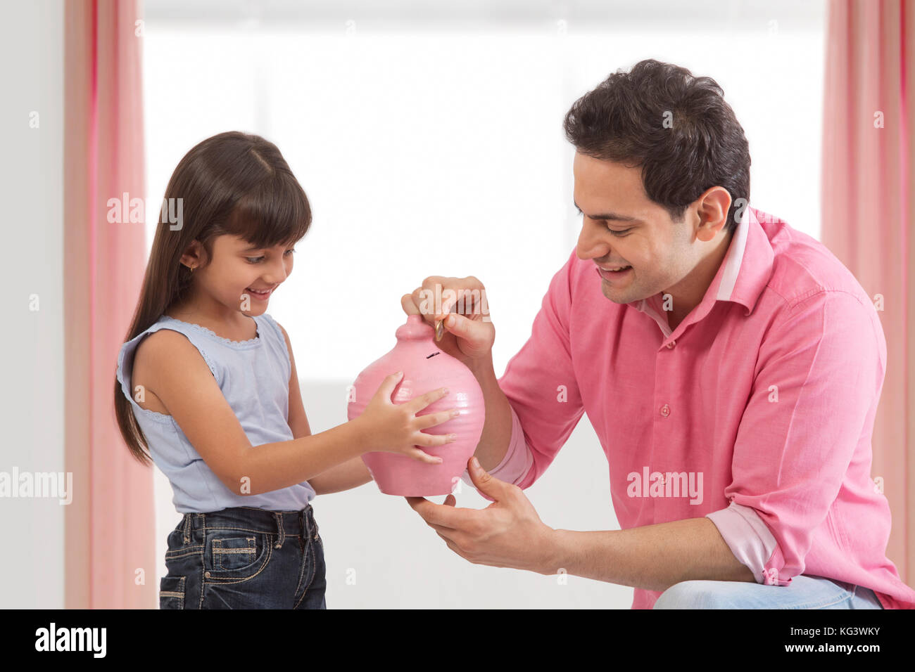 Father and daughter putting coin in piggy bank Stock Photo - Alamy