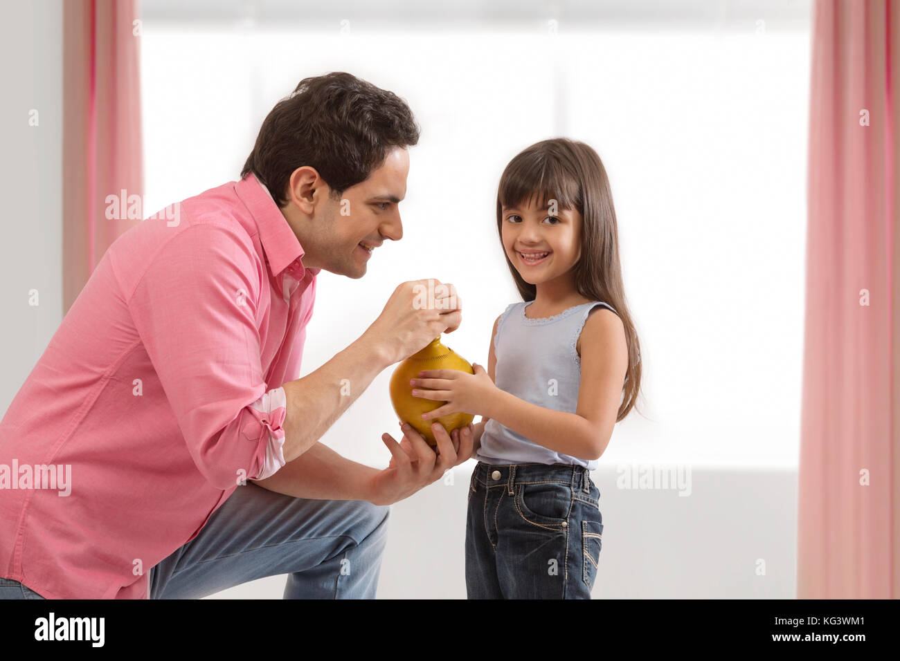 Father and daughter inserting coin in piggy bank Stock Photo - Alamy