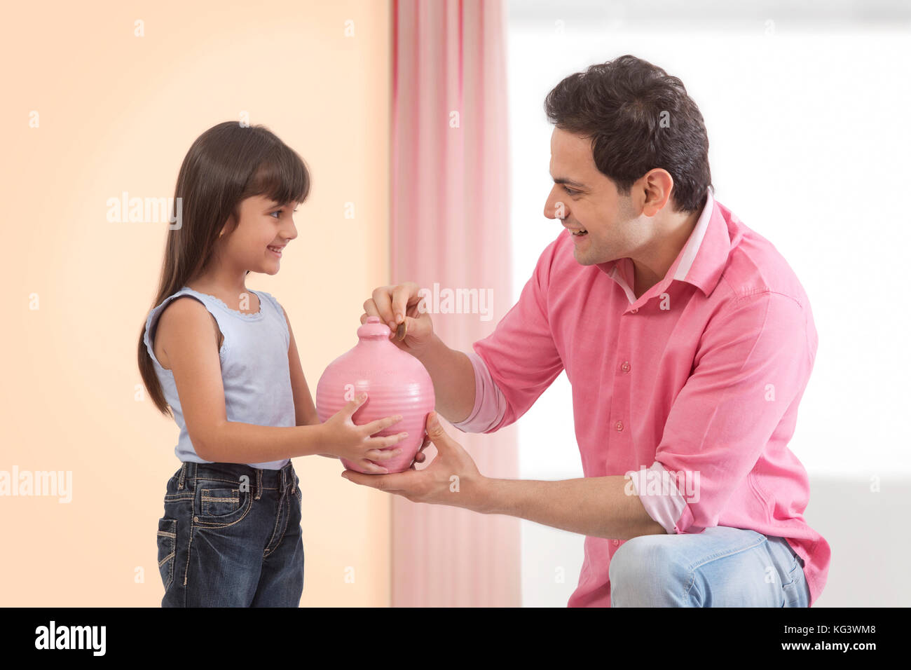 Father and daughter inserting coin in piggy bank Stock Photo - Alamy