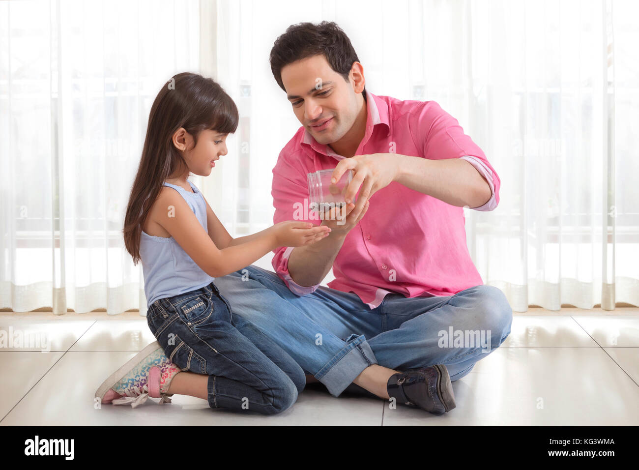 Father pouring coins from money box in daughter hand Stock Photo