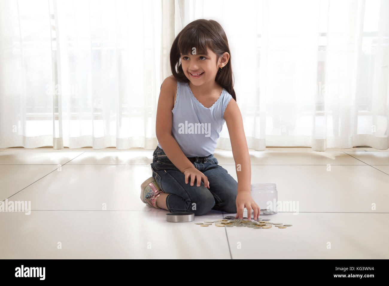little girl with coin box and coins on floor Stock Photo
