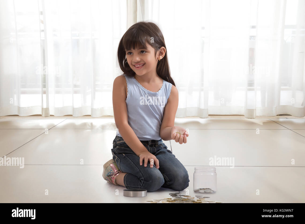little girl with coin box and coins on floor Stock Photo