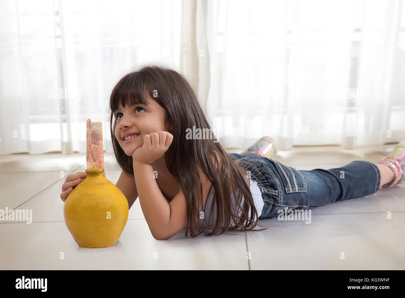 Little girl thinking lying on floor with piggy bank Stock Photo