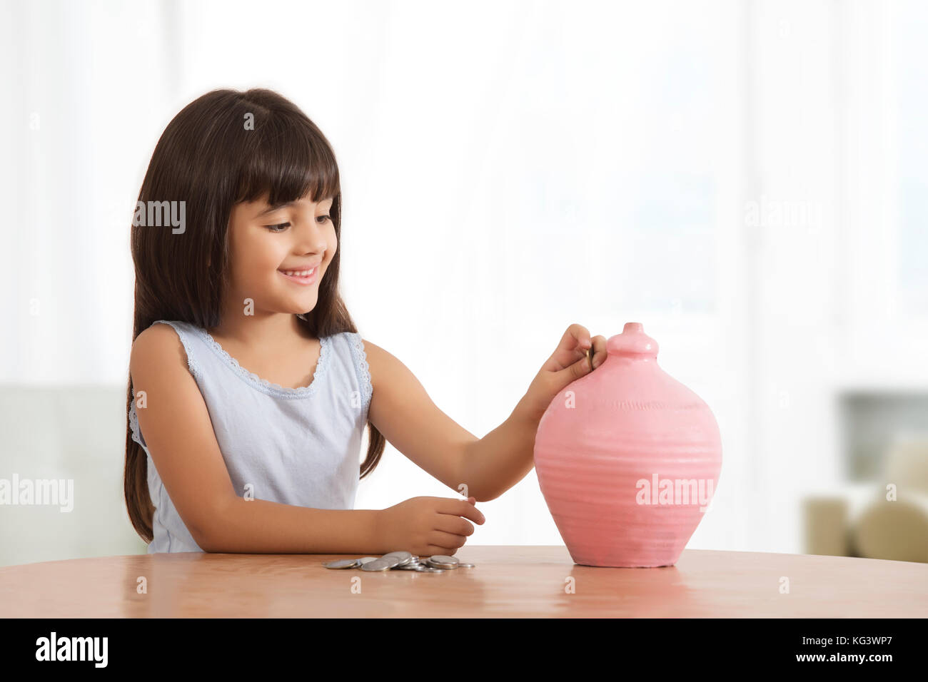 Portrait of little girl putting coins in clay piggy bank Stock Photo