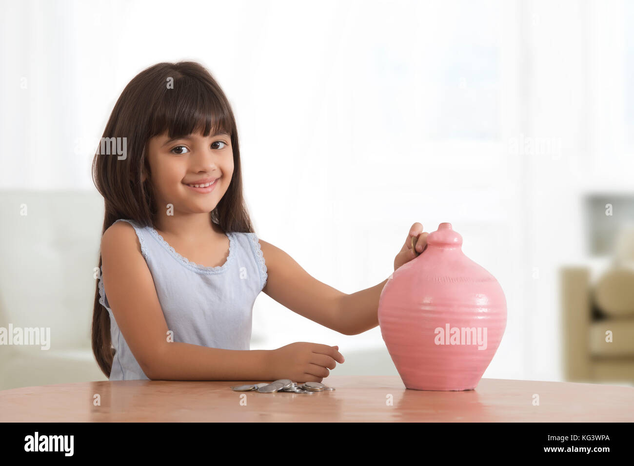 Portrait of little girl inserting coins in clay piggy bank Stock Photo