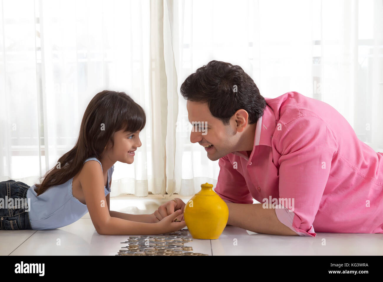 Father and daughter lying on floor with piggy bank counting change Stock Photo