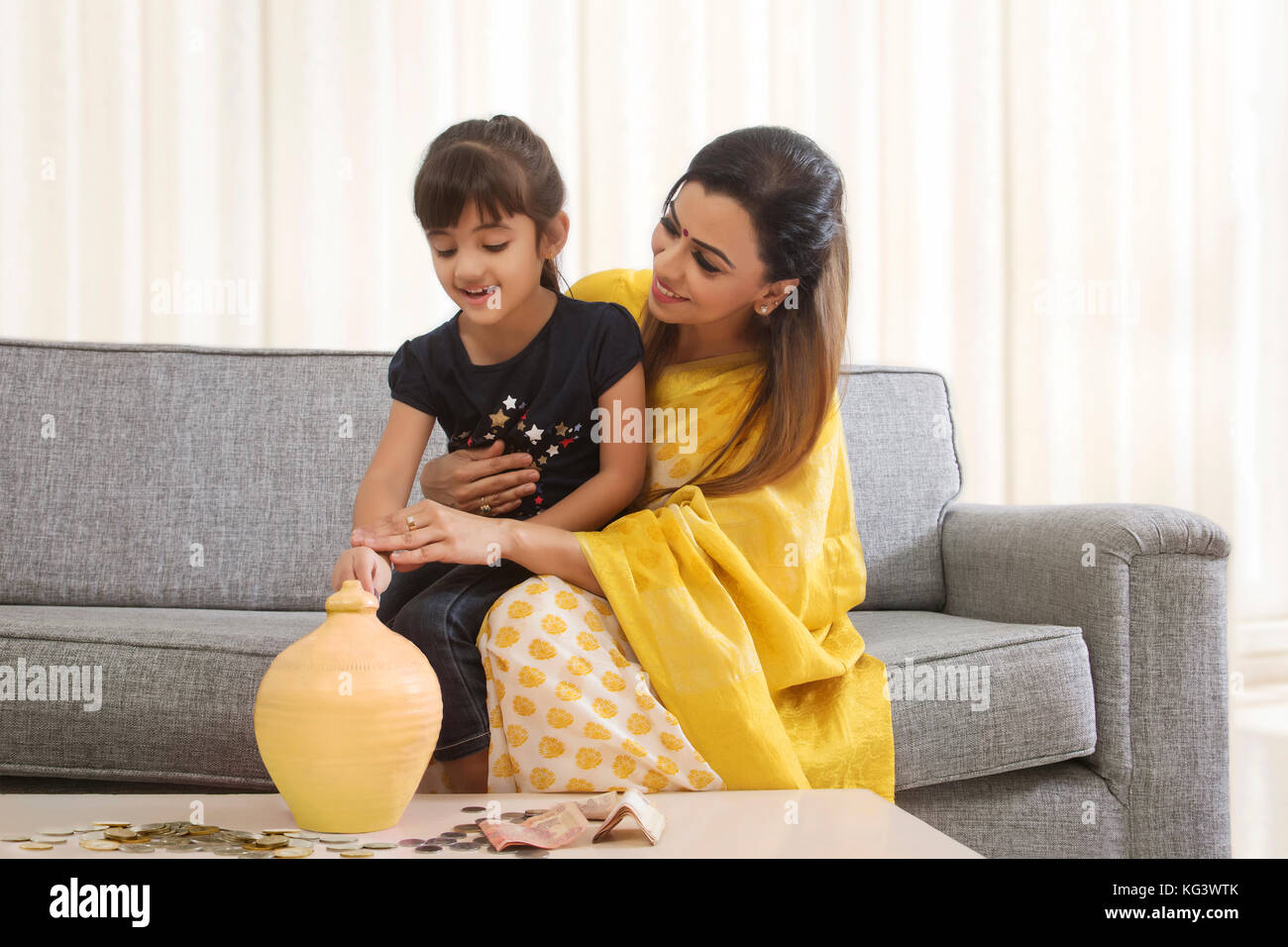 Mother and daughter putting coins in piggy bank Stock Photo - Alamy