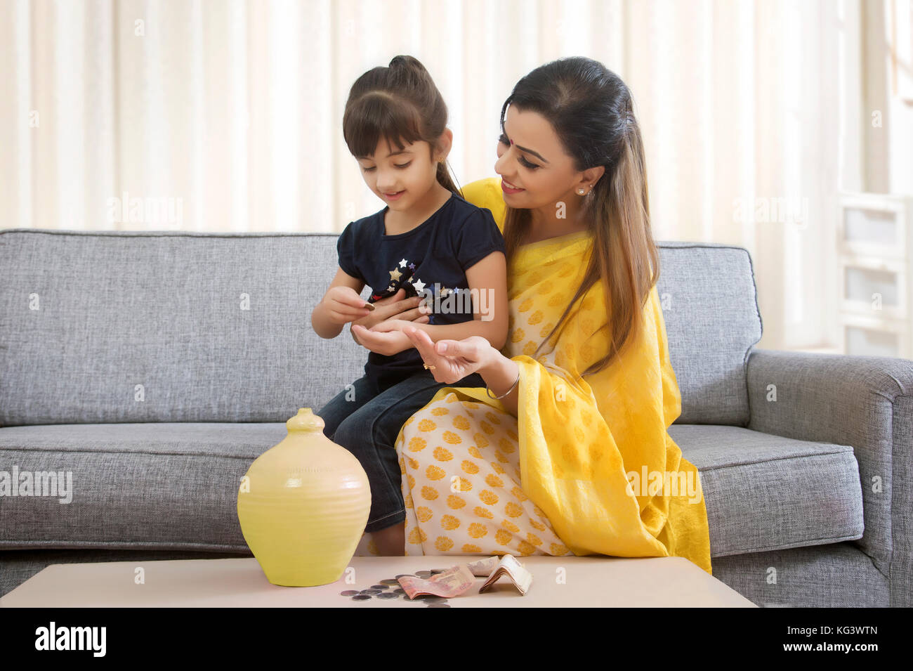 Mother and daughter inserting coins in clay piggy bank Stock Photo - Alamy