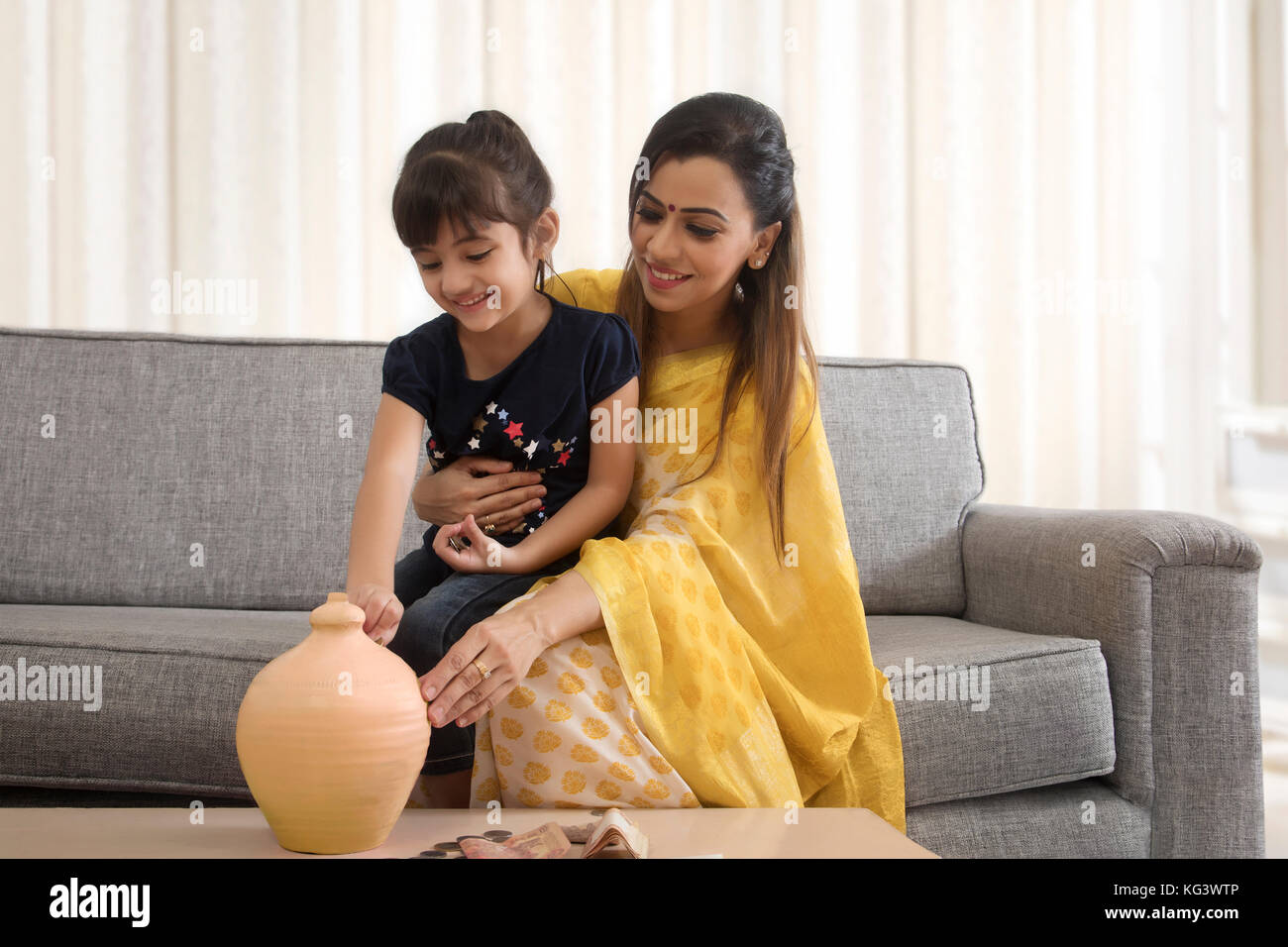 Mother and daughter putting coins in piggy bank Stock Photo - Alamy