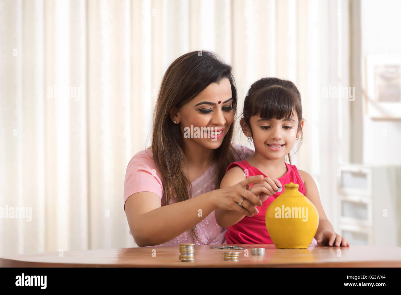 Mother and daughter putting coins in piggy bank Stock Photo - Alamy