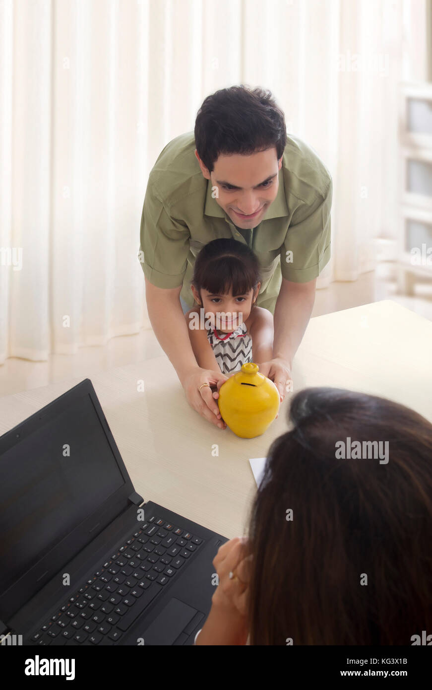 Father and daughter holding piggy bank and mother working on laptop ...