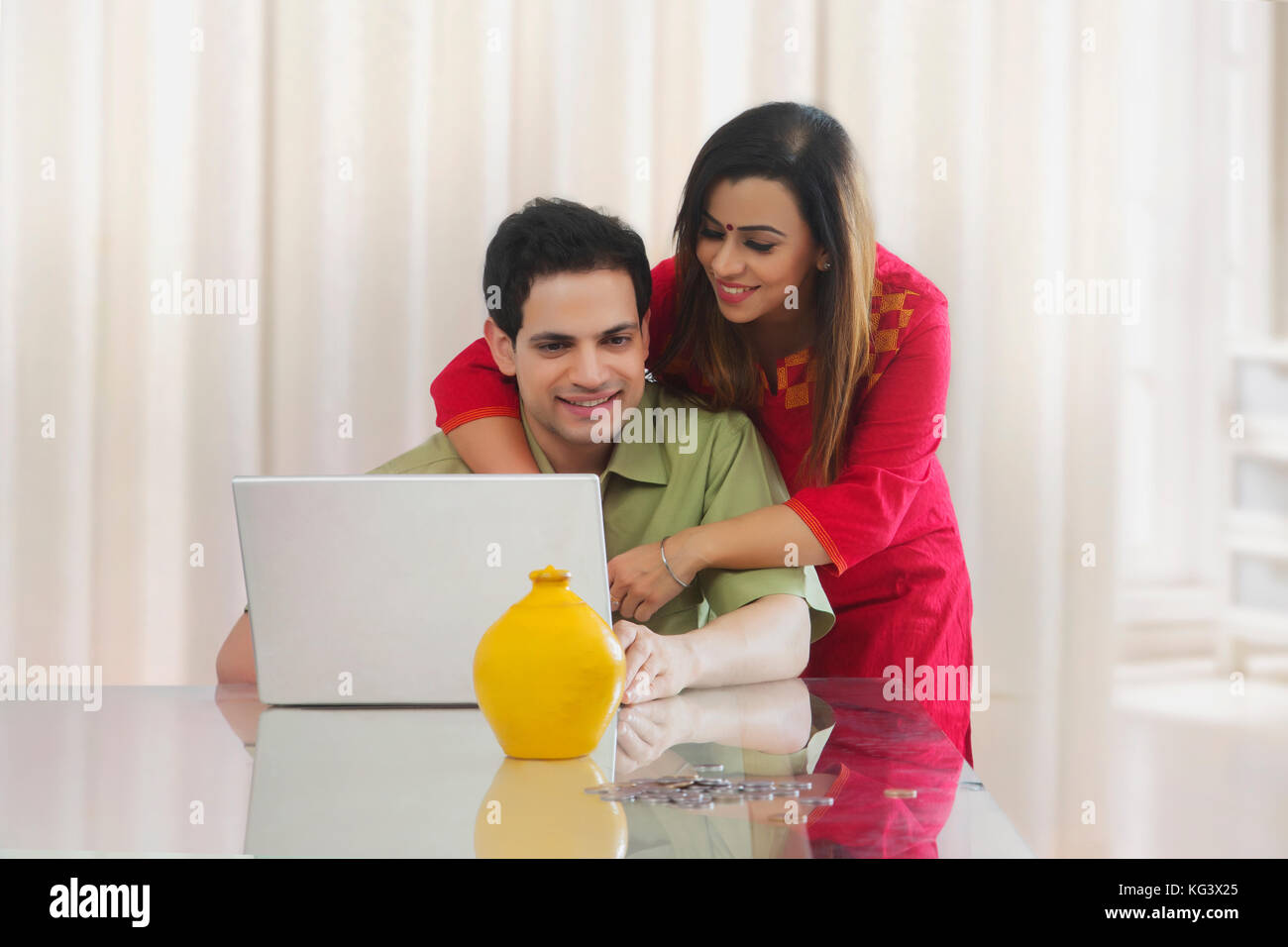 Couple looking at laptop with coins and piggy bank on table Stock Photo