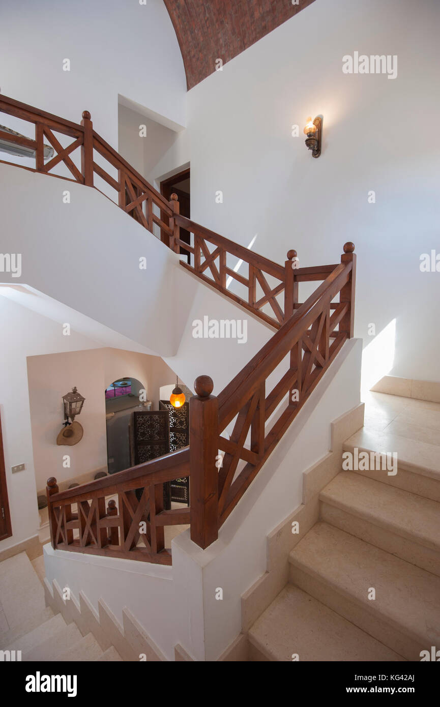 Marble curved staircase from ground floor to upstairs in luxury holiday villa with wooden bannister railing Stock Photo