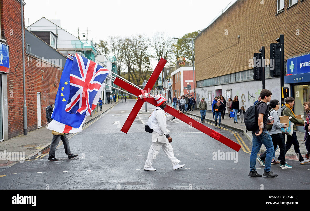 Brighton, UK. 4th November, 2017. A man with a large red cross and various flags including the Europe stars walks through Brighton city centre on a dull but warm Autumn afternoon but temperatures are forecast to plummet over the next few days throughout Britain Photograph taken by Simon Dack/Alamy Live News Stock Photo