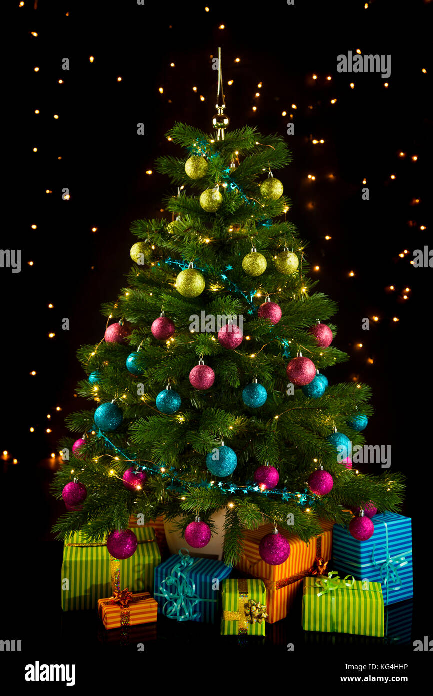 Illuminated christmas tree with gift boxes below and sparkling lights in background Stock Photo