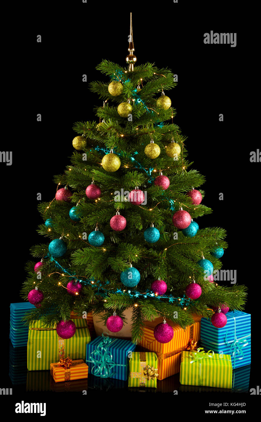 Illuminated christmas tree with colorful baubles, christmas gifts below, on black background Stock Photo