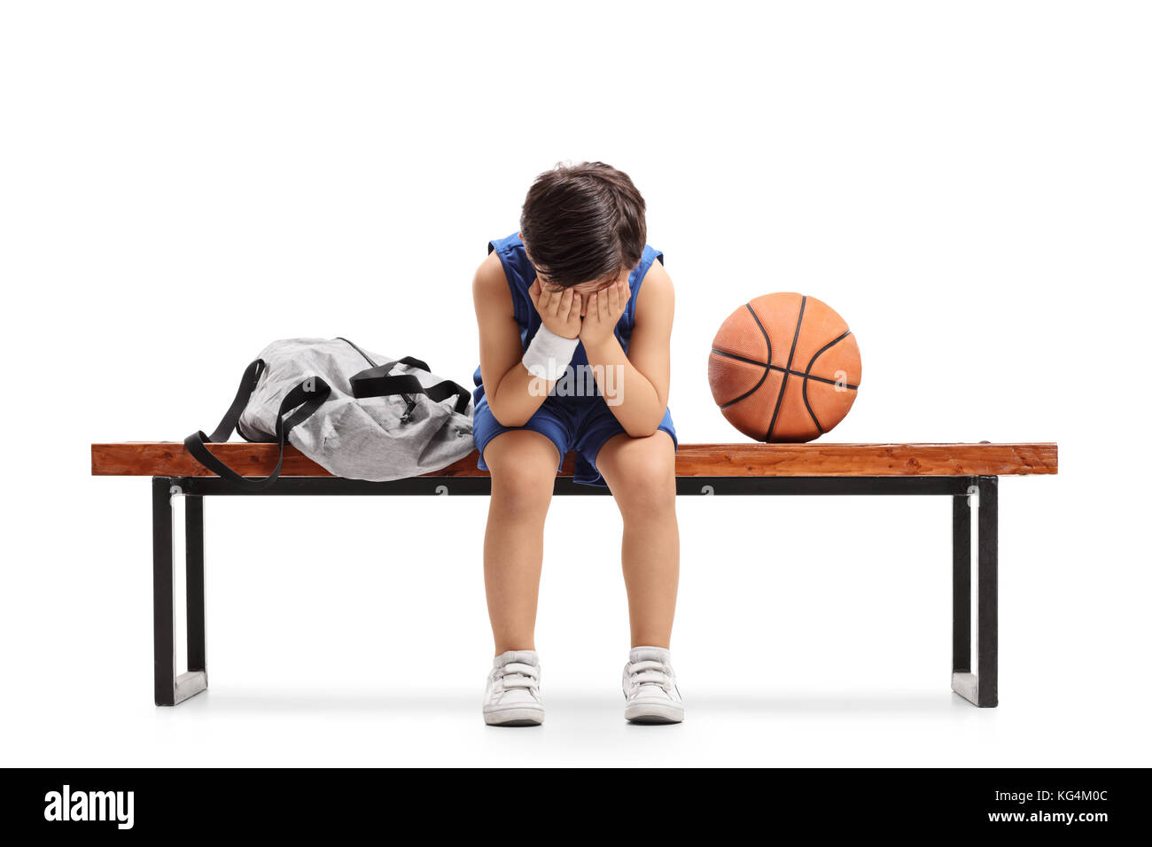 Sad little basketball player sitting on a bench and crying isolated on white background Stock Photo