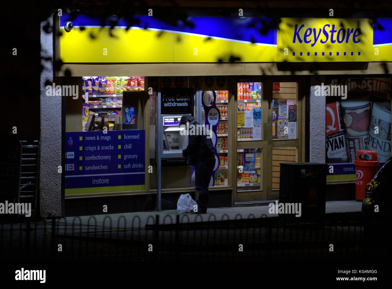 man using paypoint cash machine at convenience store at night viewed from behind Stock Photo