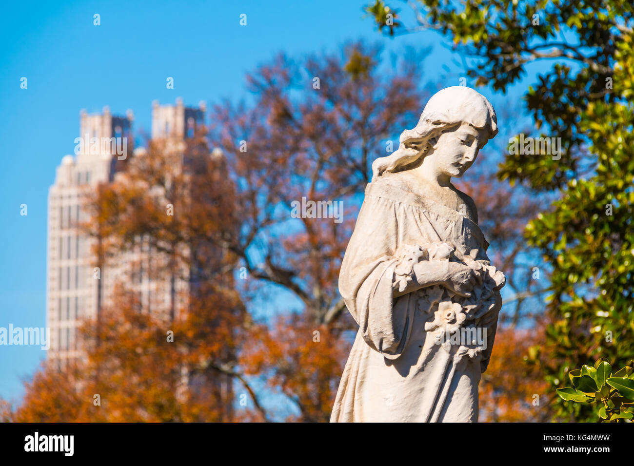 The sculpture of Virgin Mary closeup on the Oakland Cemetery on the background of skyscraper in sunny autumn day, Atlanta, USA Stock Photo