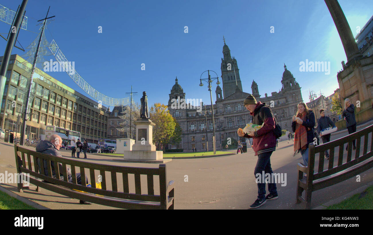 locals and tourists eating fast food fish and chips enjoy sitting in the sun on the benches in george square in a perspective fish eye lens shot Stock Photo